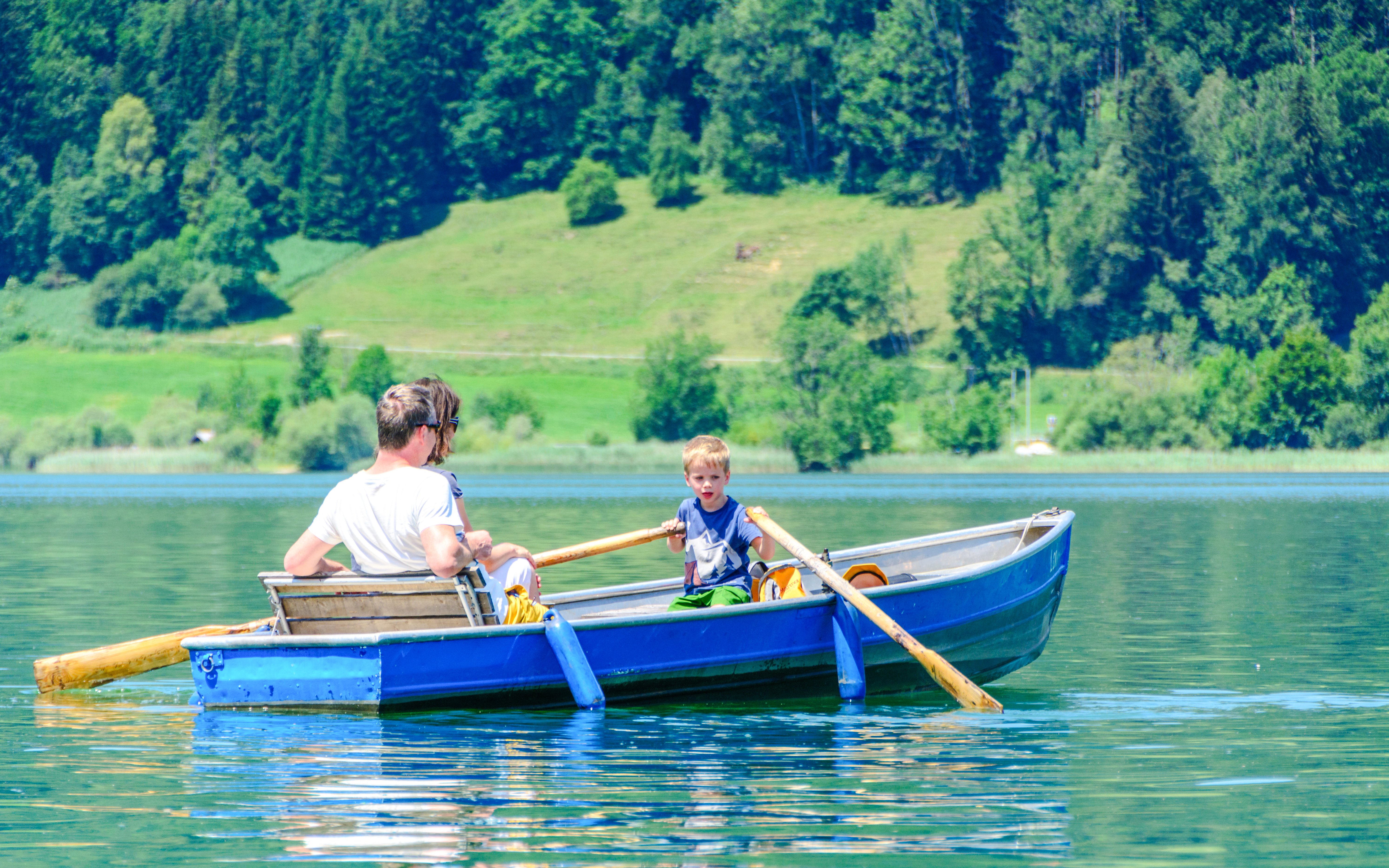 Rowboat on Alpsee Lake with child rowing, surrounded by lush green forest.