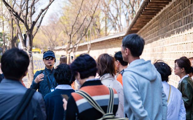 Tour guide leading a group along a historic Korean wall on a walking tour.