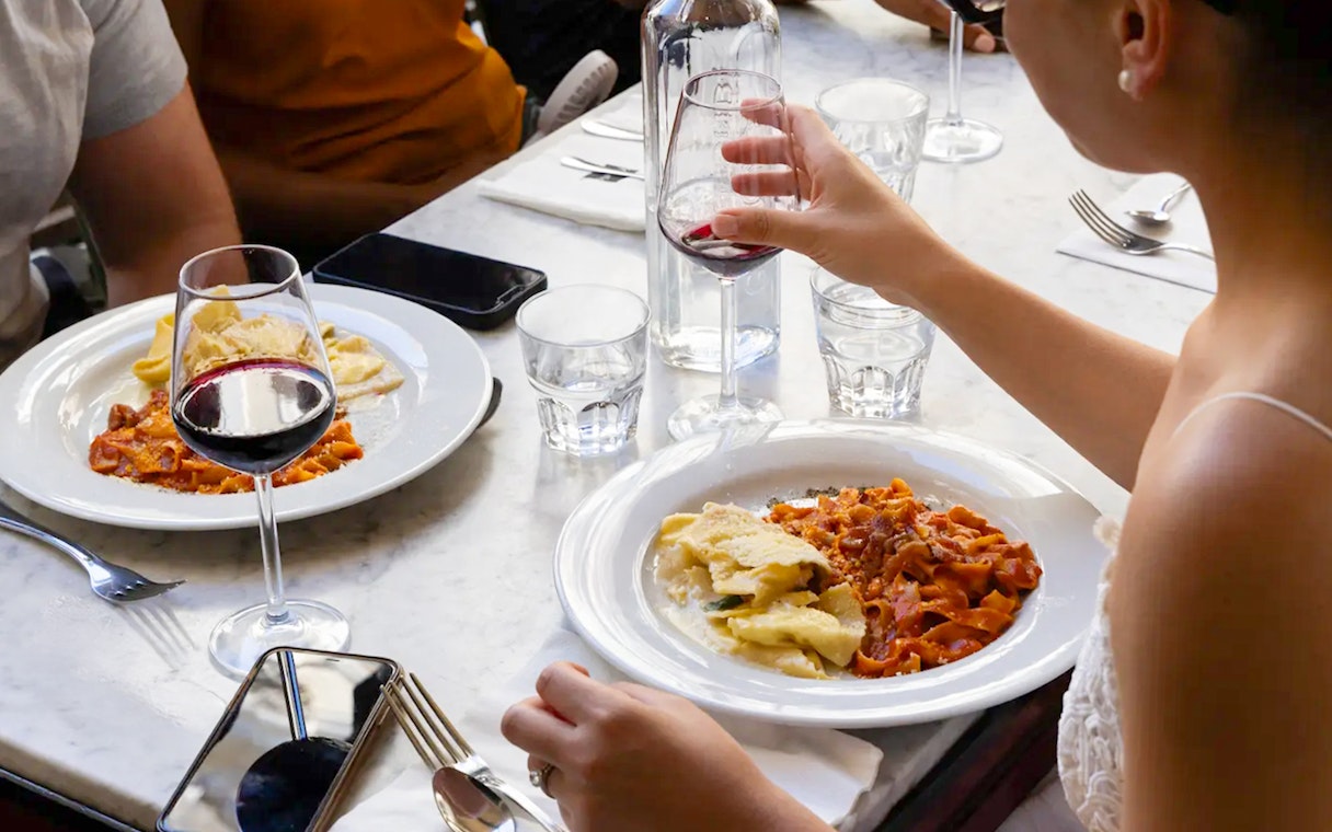 People enjoying pasta and red wine at a restaurant table.