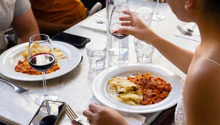 People enjoying pasta and red wine at a restaurant table.