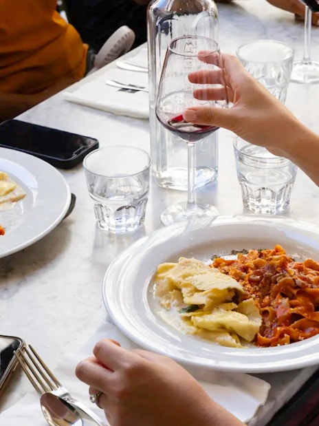 People enjoying pasta and red wine at a restaurant table.