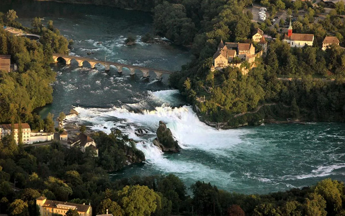 Rhine Falls with surrounding greenery and historic buildings in Switzerland.