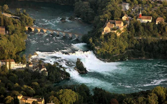 Rhine Falls with surrounding greenery and historic buildings in Switzerland.