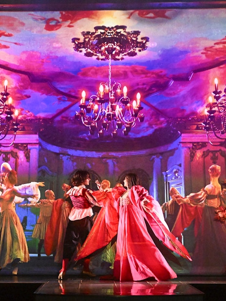 Dancers in vibrant costumes perform on stage at a Paris cabaret with ornate backdrop.
