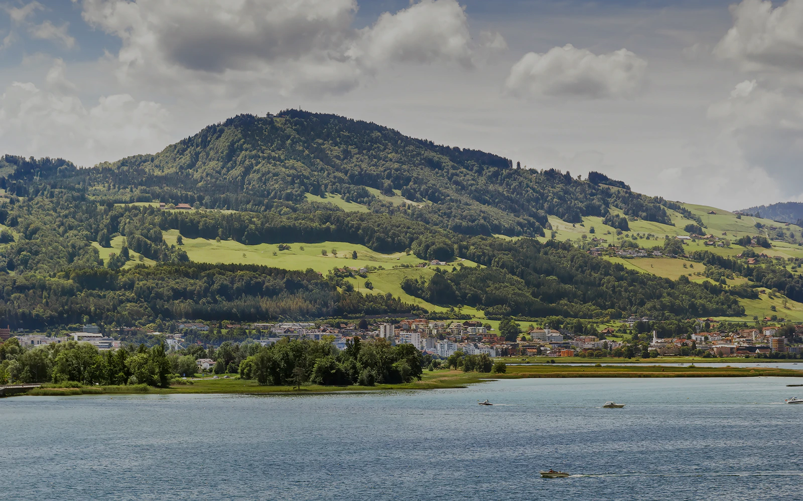 Zurich cityscape with boats on Lake Zurich and lush hills in the background.
