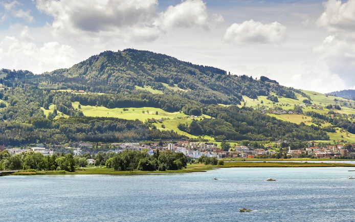 Zurich cityscape with boats on Lake Zurich and lush hills in the background.