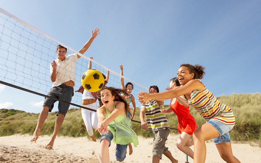Teenage friends playing volleyball on Moreton Island beach.