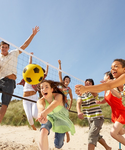Teenage friends playing volleyball on Moreton Island beach.