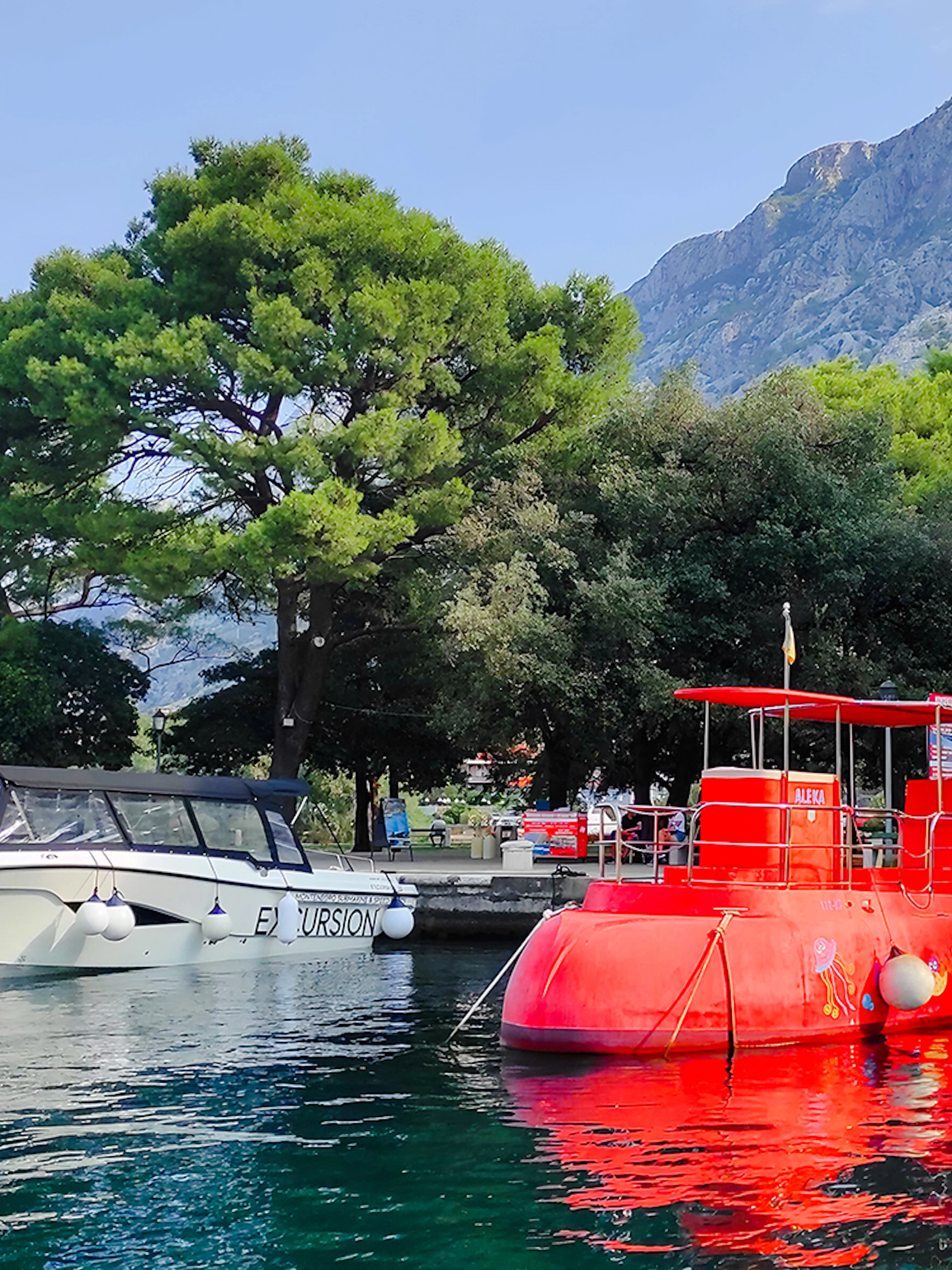 Docked red semi-submarine in Boka Bay, Kotor, with mountains and trees in the background.