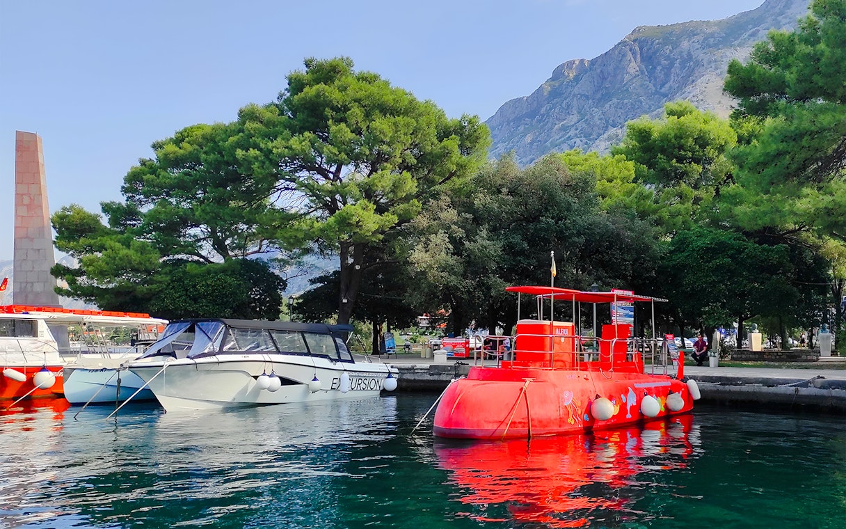Docked red semi-submarine in Boka Bay, Kotor, with mountains and trees in the background.