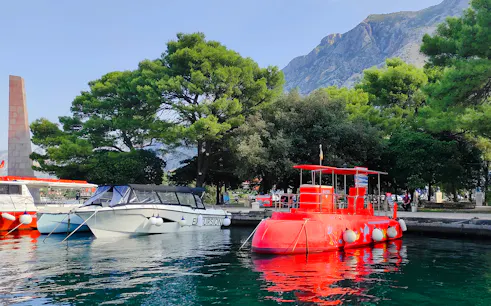 Docked red semi-submarine in Boka Bay, Kotor, with mountains and trees in the background.