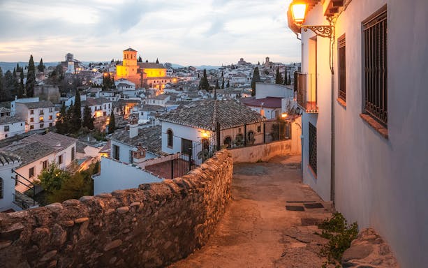 Alleyway in Albaicín, Granada, with illuminated historic buildings at dusk.