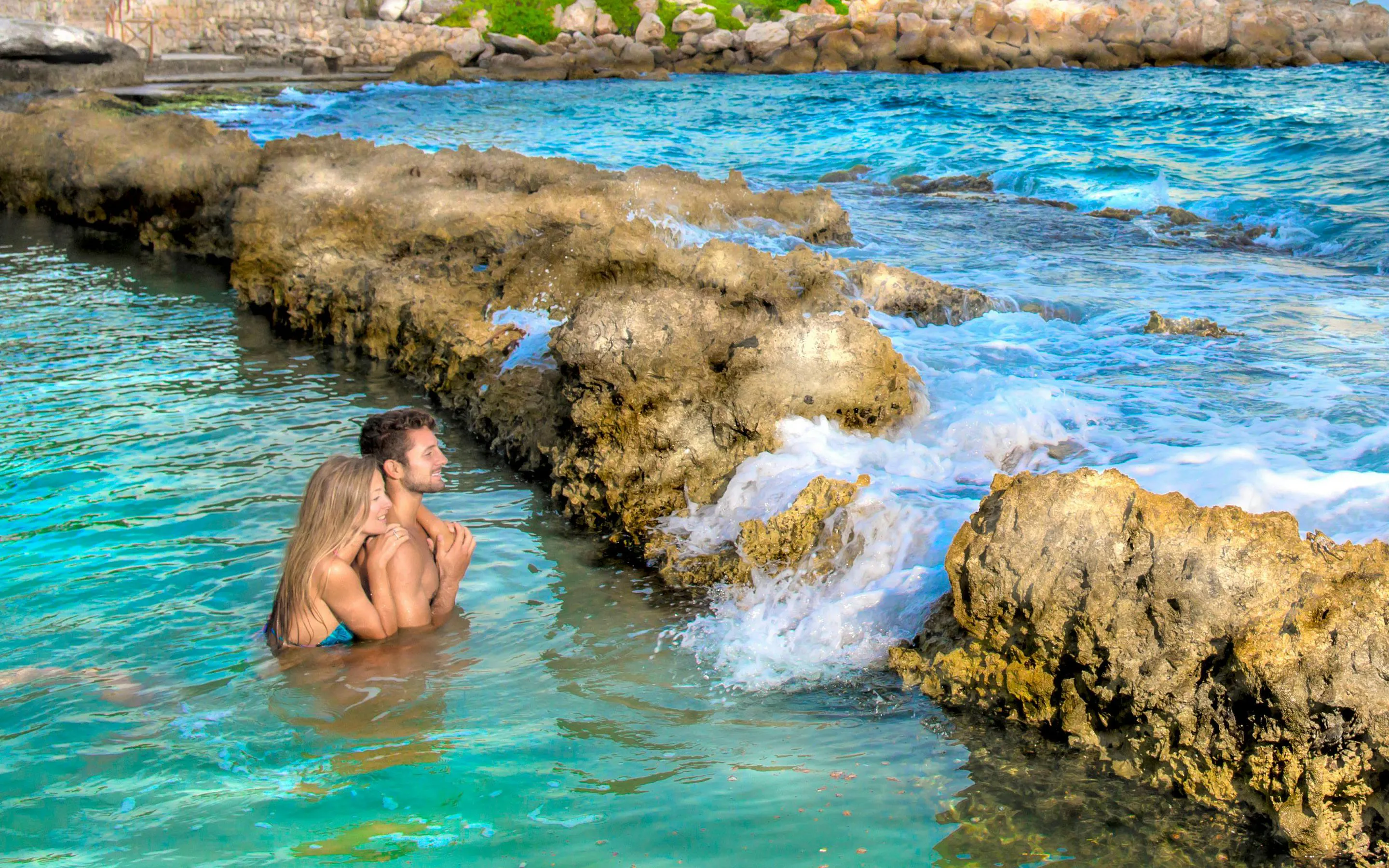 Couple enjoying the natural pools at Xcaret Park, surrounded by rocky formations.