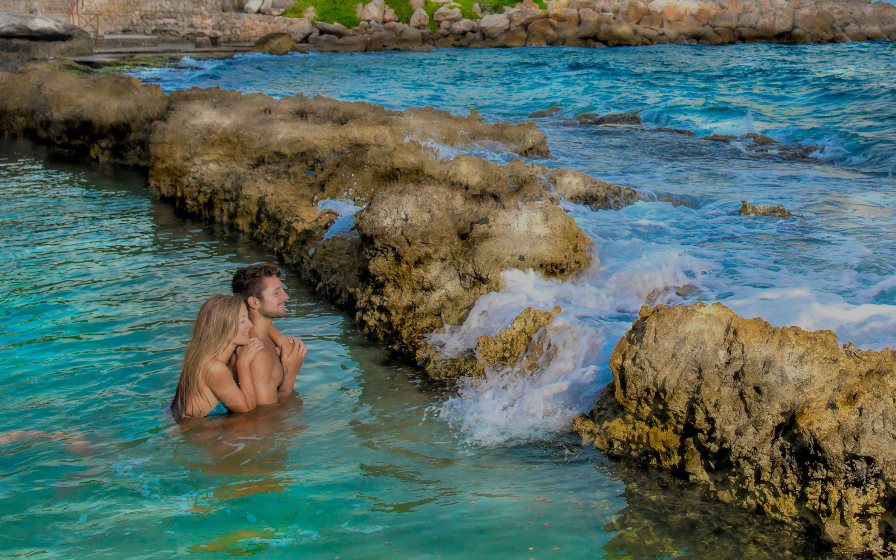 Couple enjoying the natural pools at Xcaret Park, surrounded by rocky formations.