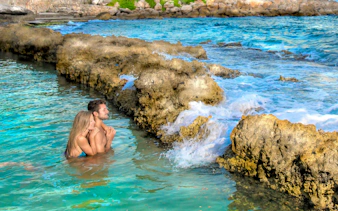 Couple enjoying the natural pools at Xcaret Park, surrounded by rocky formations.