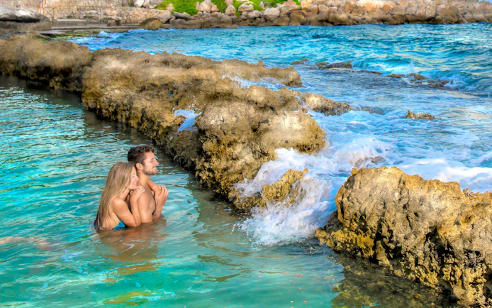 Couple enjoying the natural pools at Xcaret Park, surrounded by rocky formations.
