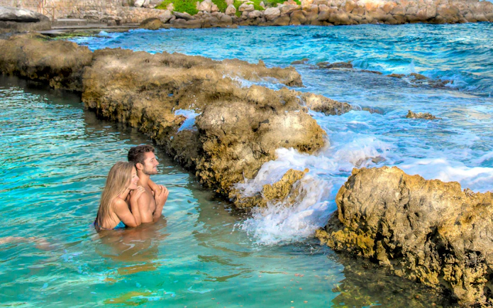 Couple enjoying the natural pools at Xcaret Park, surrounded by rocky formations.