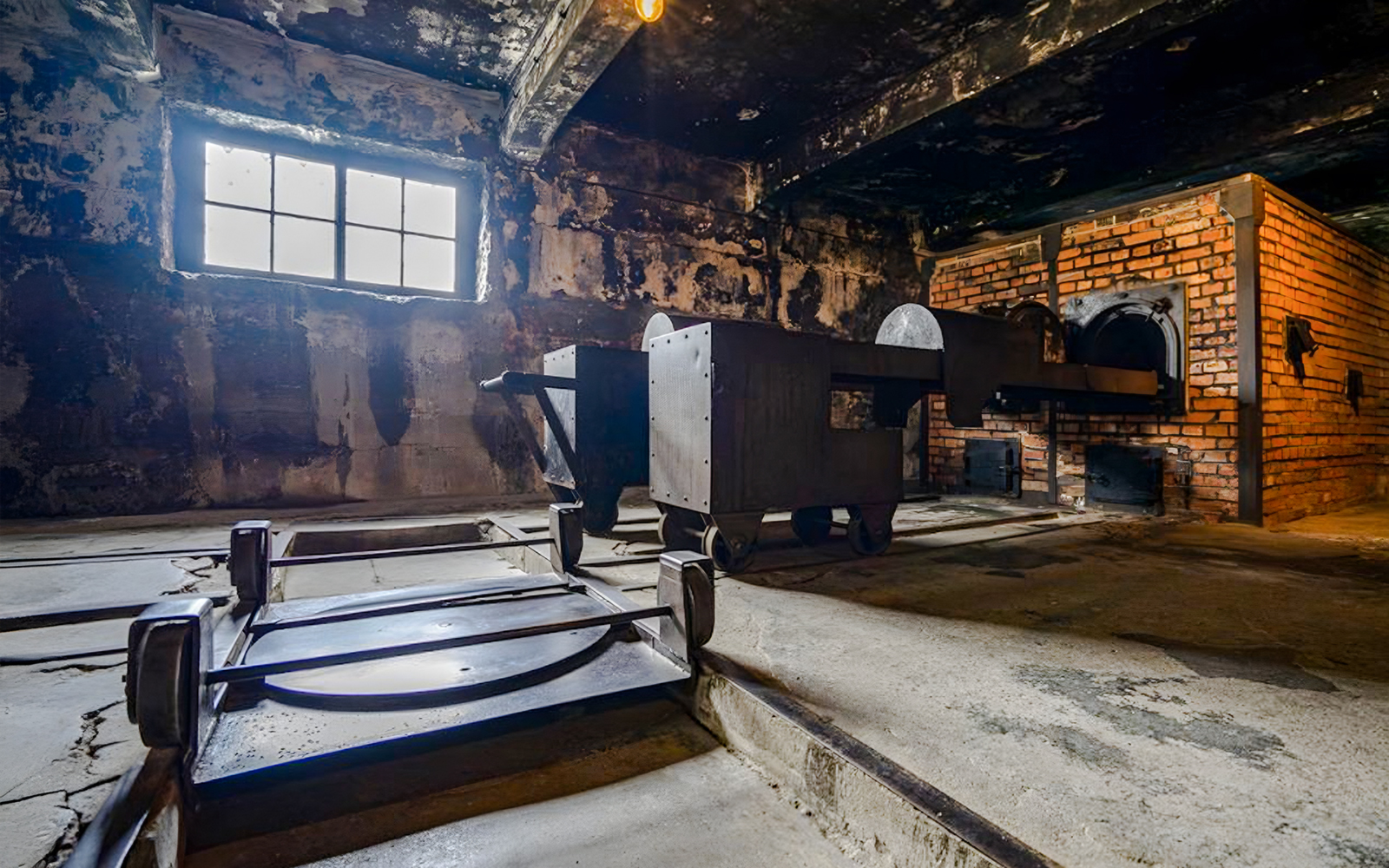 Crematorium interior at Auschwitz I, showing brick ovens and metal carts.