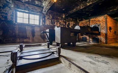 Crematorium interior at Auschwitz I, showing brick ovens and metal carts.