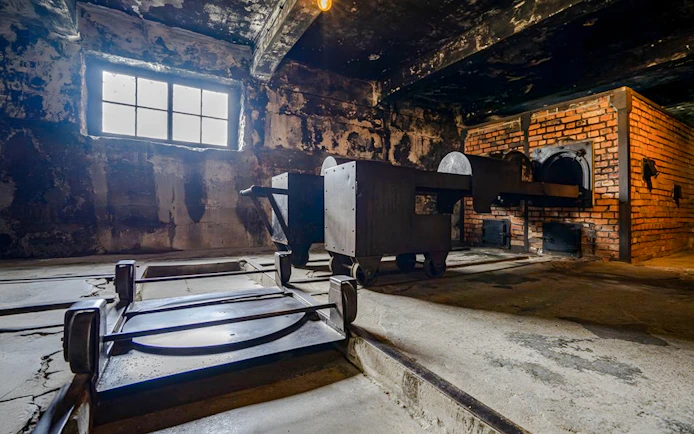 Crematorium interior at Auschwitz I, showing brick ovens and metal carts.