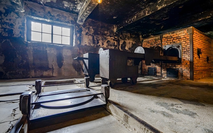 Crematorium interior at Auschwitz I, showing brick ovens and metal carts.