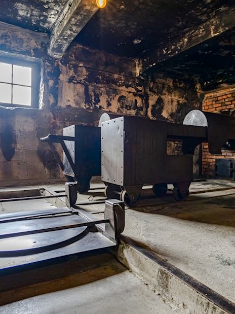 Crematorium interior at Auschwitz I, showing brick ovens and metal carts.
