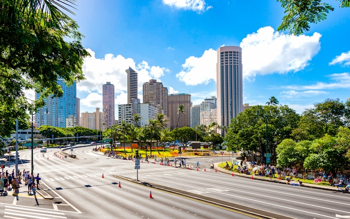 Waikiki skyline with high-rise buildings and palm trees, seen from a busy street in Oahu, Hawaii.