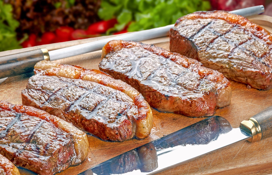 Sliced picanha on a wooden board at a steakhouse rotisserie.