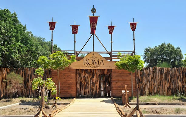 Entrance to Roma World theme park with wooden gate and red banners.