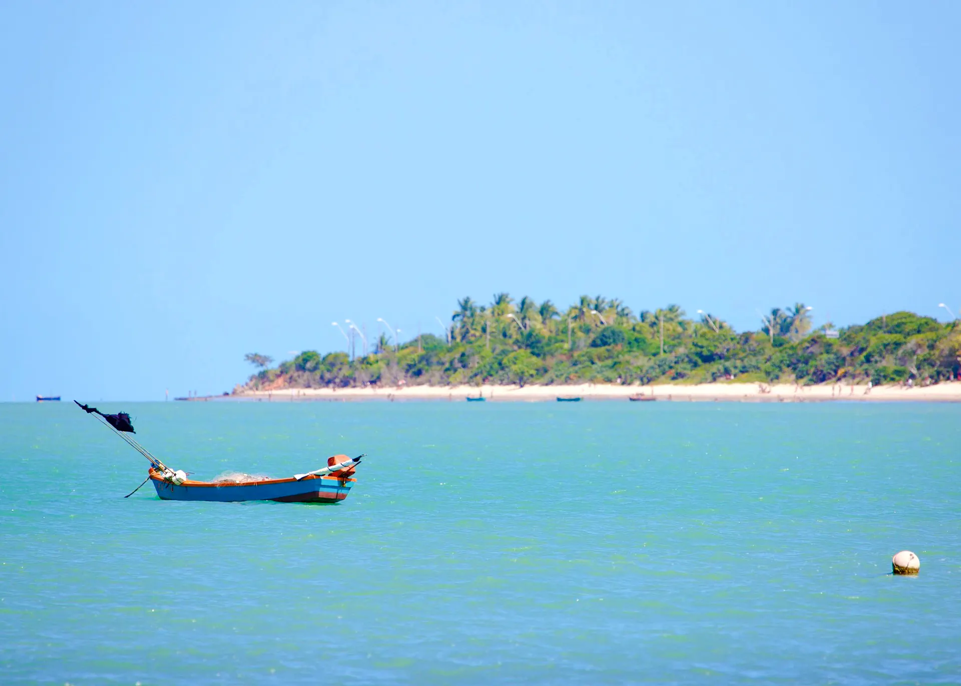 Boat on turquoise water near Coroa Vermelha beach, Porto Seguro, with lush greenery in the background.