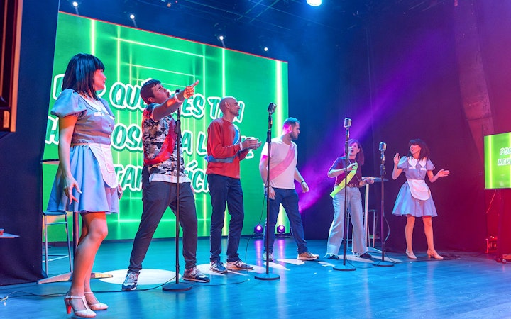 Performers on stage during "Coctel, un Musical al reves" with vibrant green backdrop.