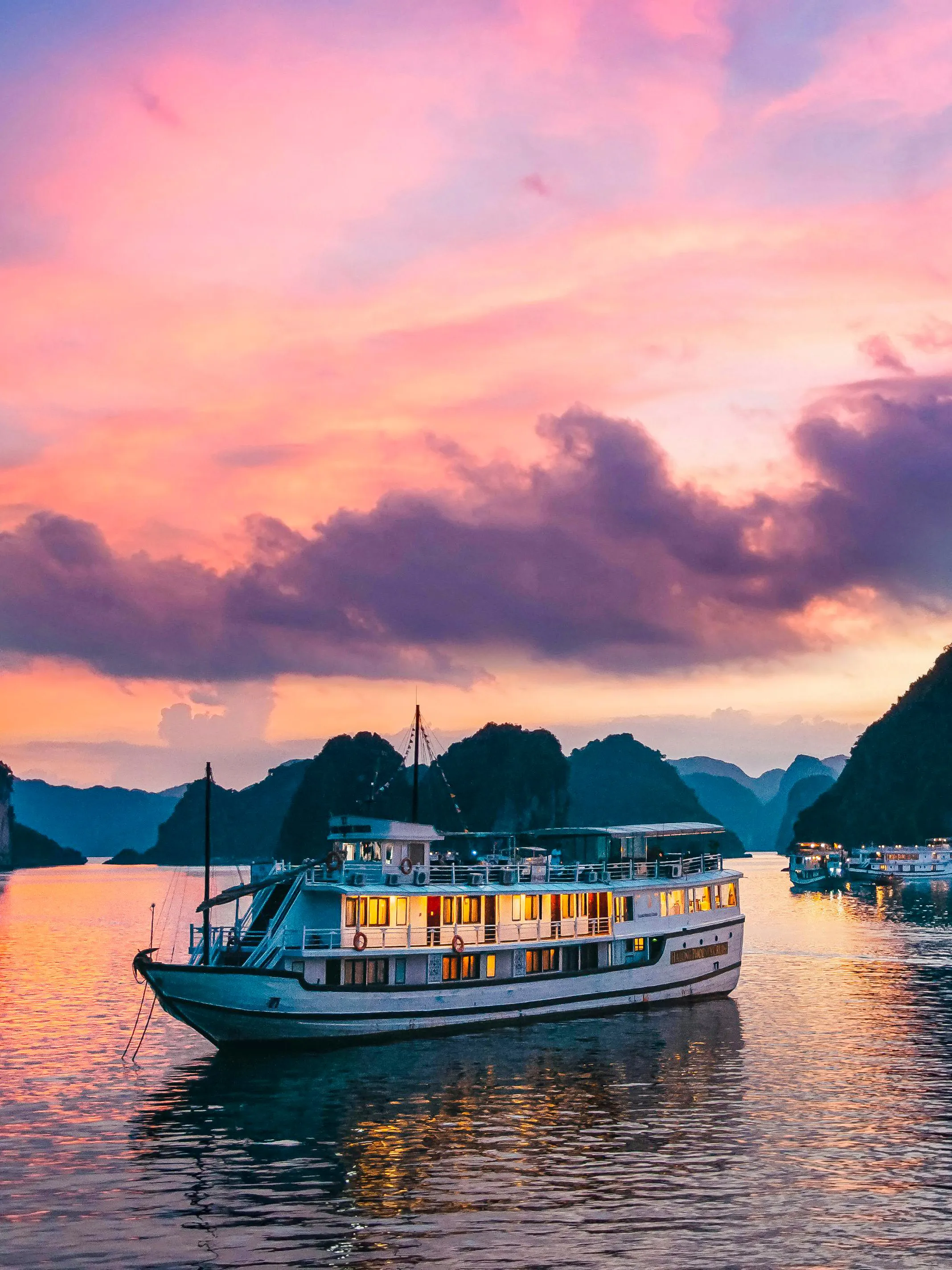 Cruise ship sailing in Ha Long Bay at sunset with limestone islands in the background.
