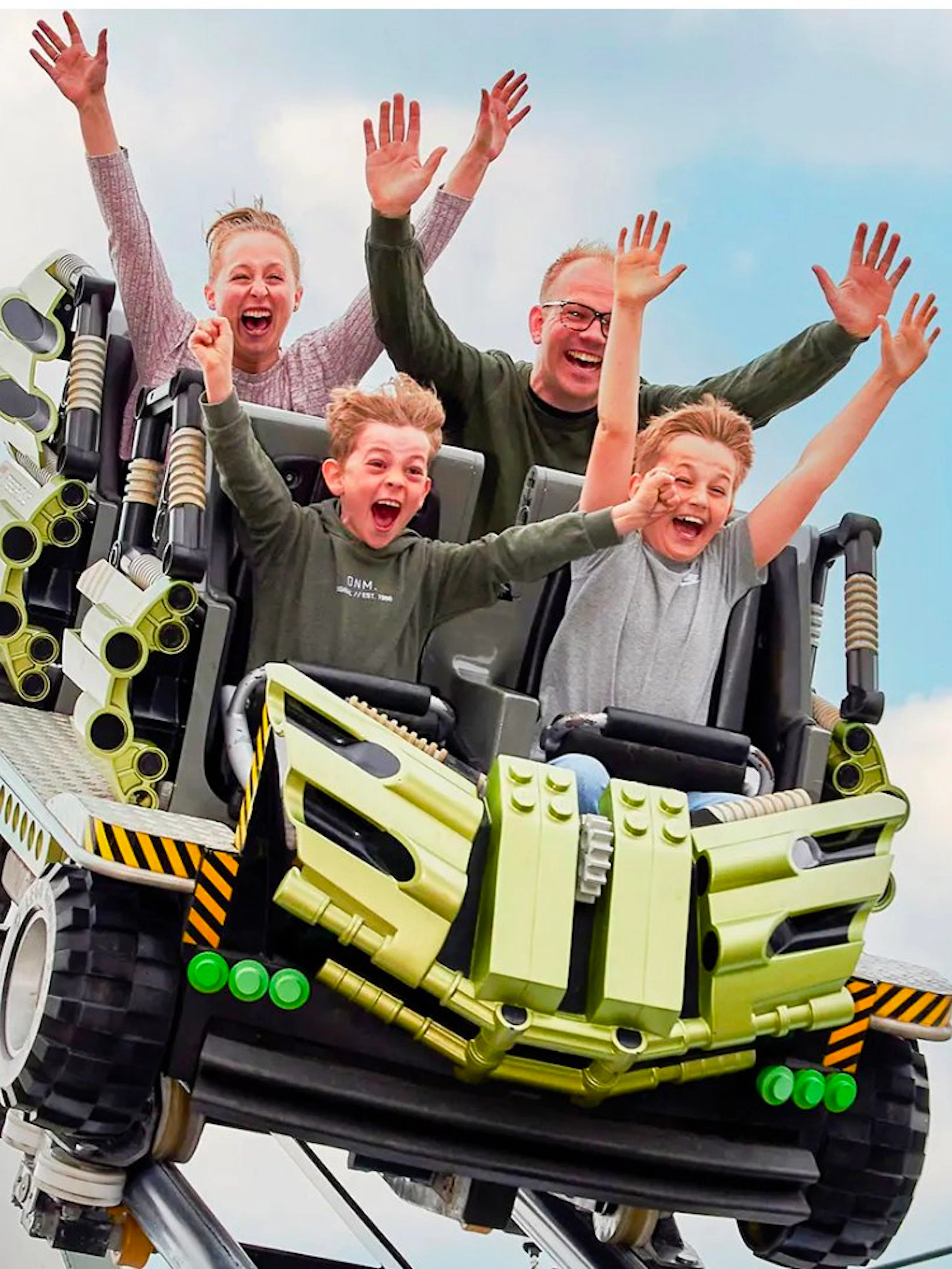 Guests riding a roller coaster at LEGOLAND Billund with hands raised in excitement.