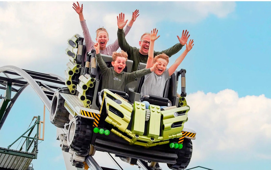 Guests riding a roller coaster at LEGOLAND Billund with hands raised in excitement.