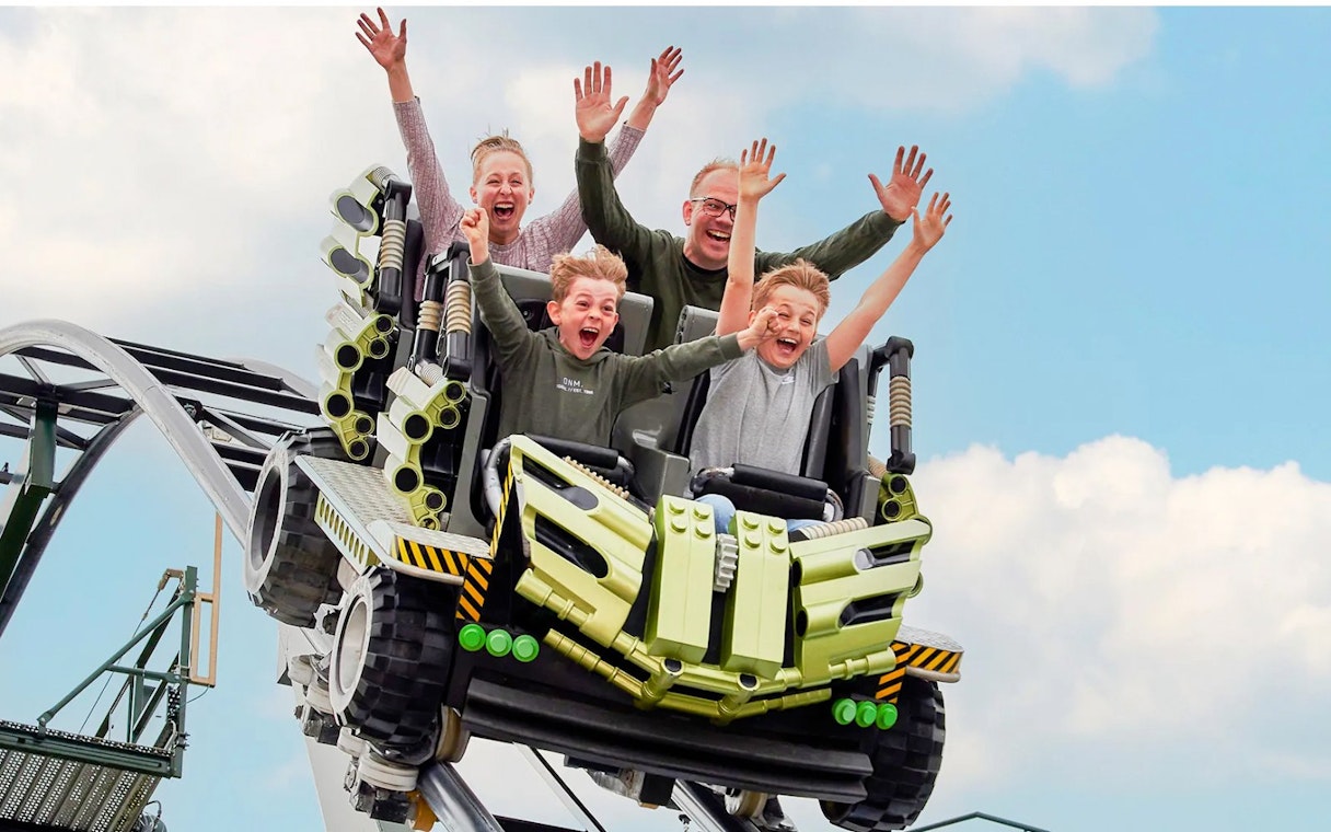 Guests riding a roller coaster at LEGOLAND Billund with hands raised in excitement.