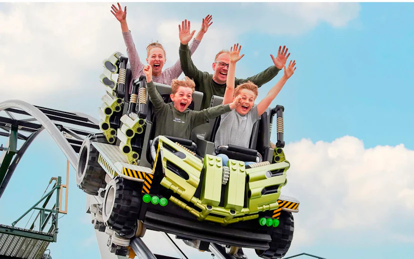 Guests riding a roller coaster at LEGOLAND Billund with hands raised in excitement.