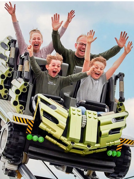 Guests riding a roller coaster at LEGOLAND Billund with hands raised in excitement.