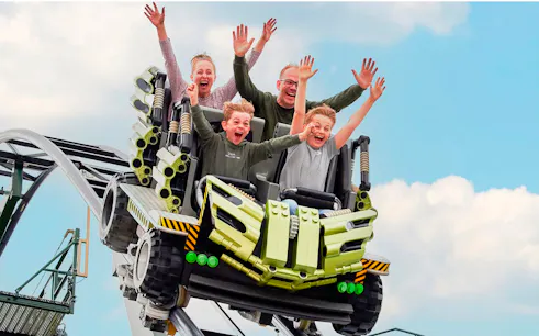 Guests riding a roller coaster at LEGOLAND Billund with hands raised in excitement.