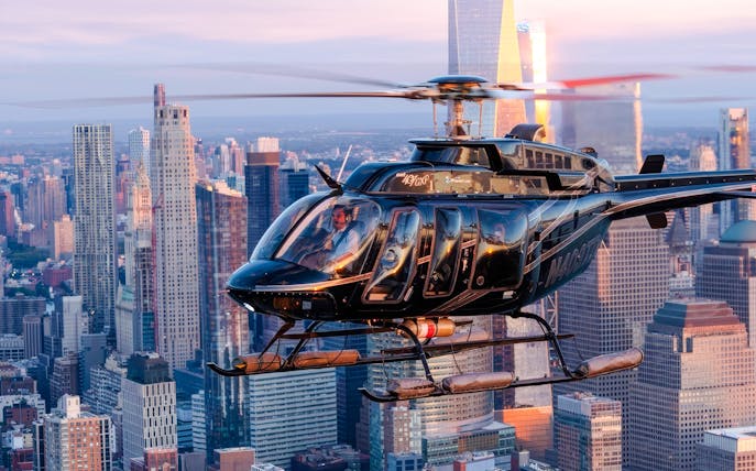 Helicopter flying over New York City skyline at sunset.