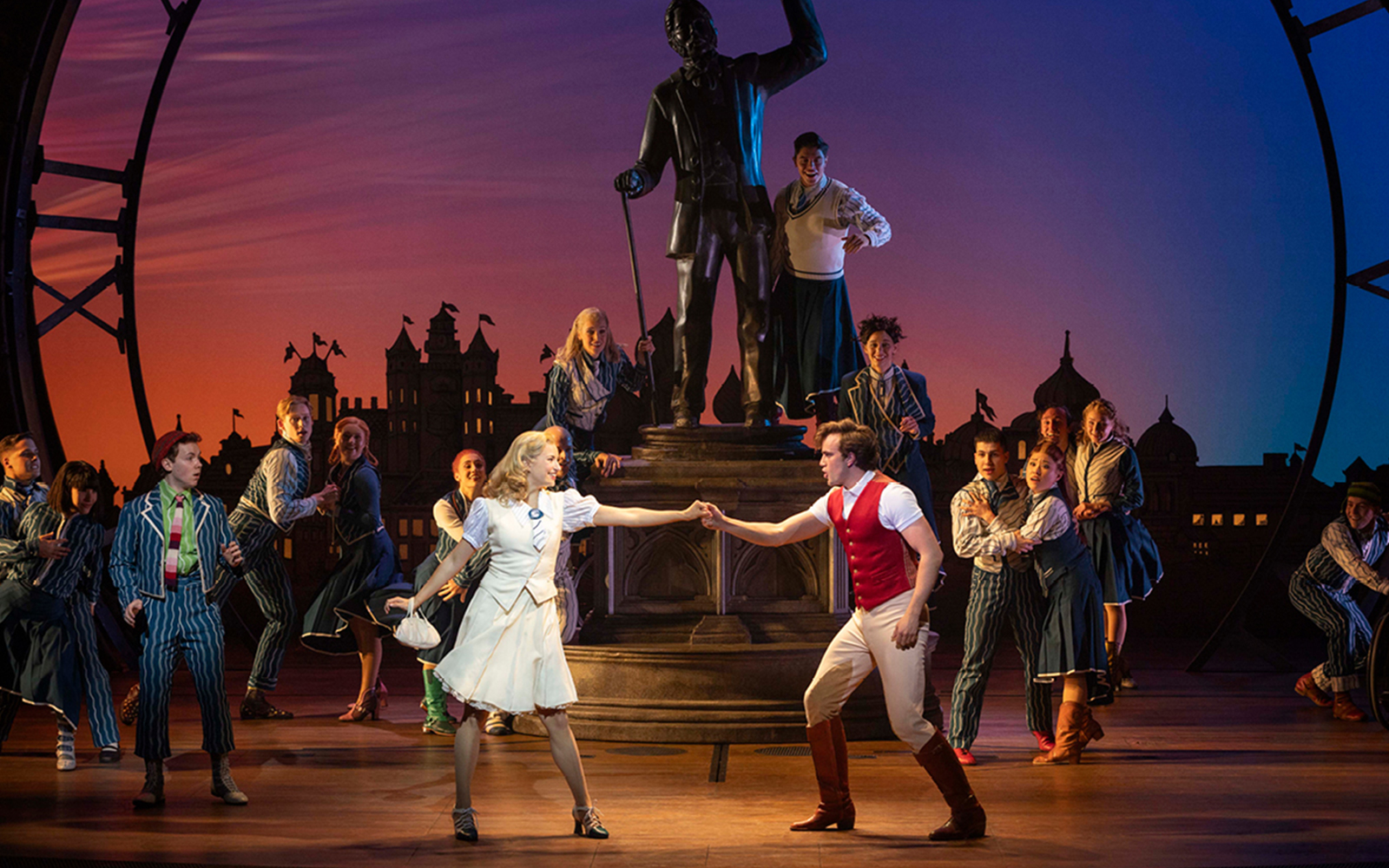 Musical cast performing a scene from Wicked with a statue backdrop.