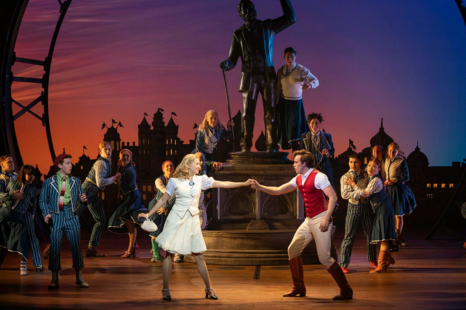Musical cast performing a scene from Wicked with a statue backdrop.
