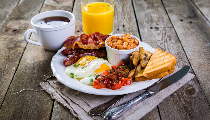 Traditional English breakfast with eggs, bacon, sausage, beans, and toast on a white plate.