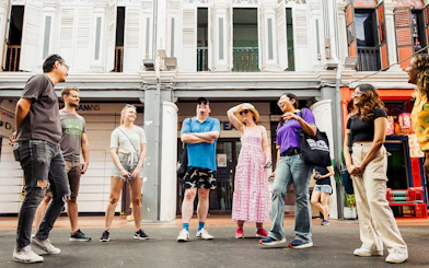 Group of tourists on a guided Michelin and local hawker food tour in a vibrant city street.