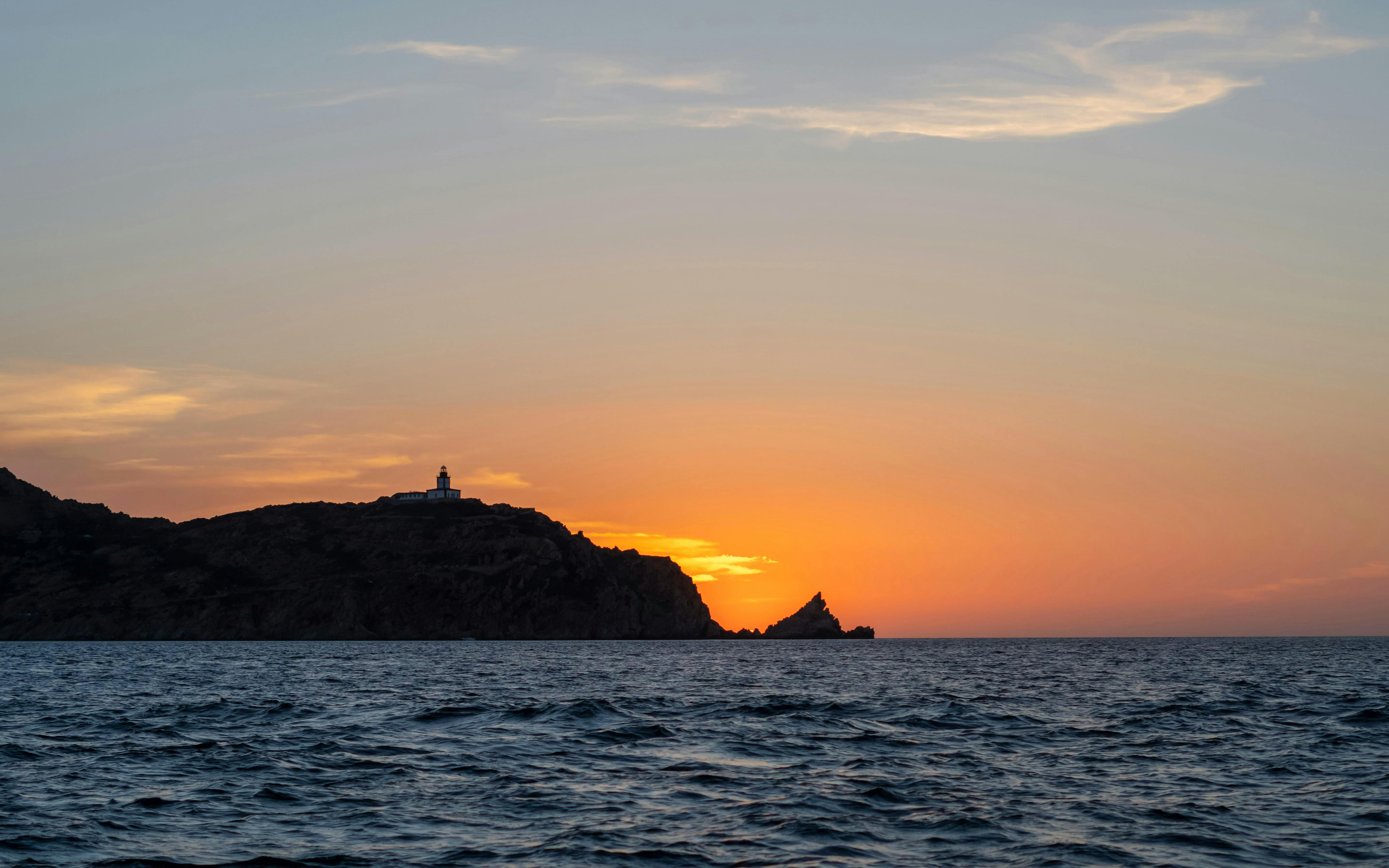 Sunset view over the sea with a lighthouse on a hill during a Marseille dinner cruise.