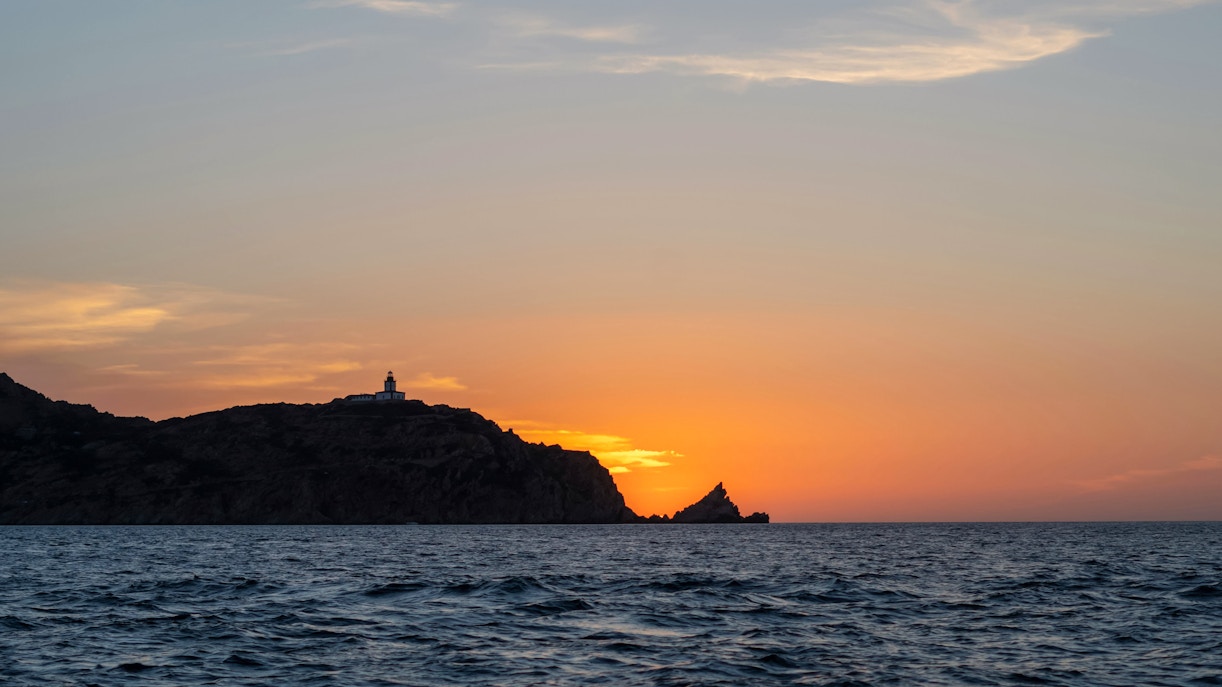 Sunset view over the sea with a lighthouse on a hill during a Marseille dinner cruise.