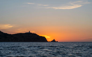 Sunset view over the sea with a lighthouse on a hill during a Marseille dinner cruise.