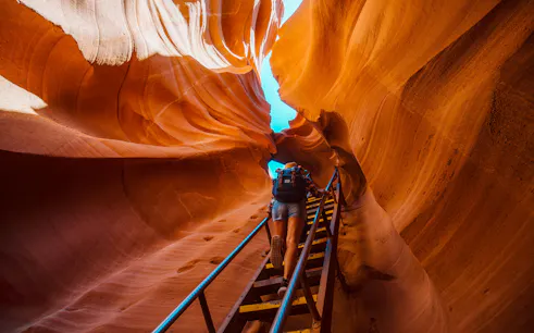 Backpacker climbing ladder in narrow Antelope Canyon passage.
