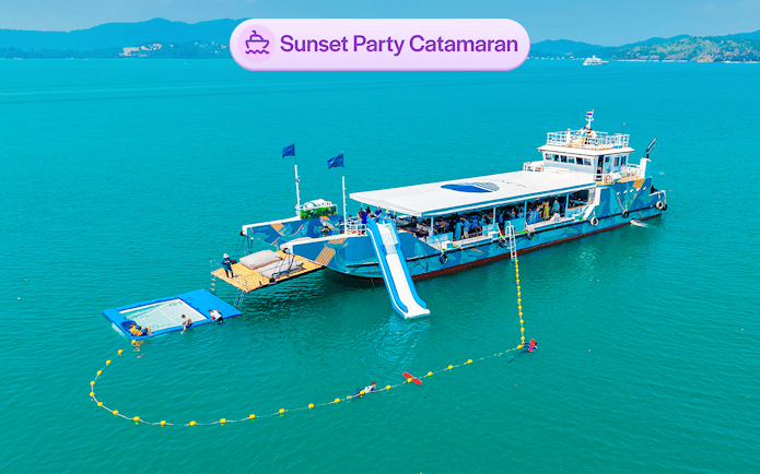 Luxury catamaran with slide and partygoers, sunset cruise near James Bond Island, Phuket.