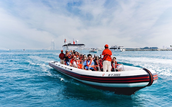 Speedboat tour with passengers near Dubai Marina, Burj Al Arab visible in the background.