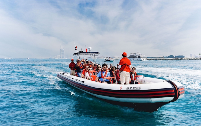 Speedboat tour with passengers near Dubai Marina, Burj Al Arab visible in the background.